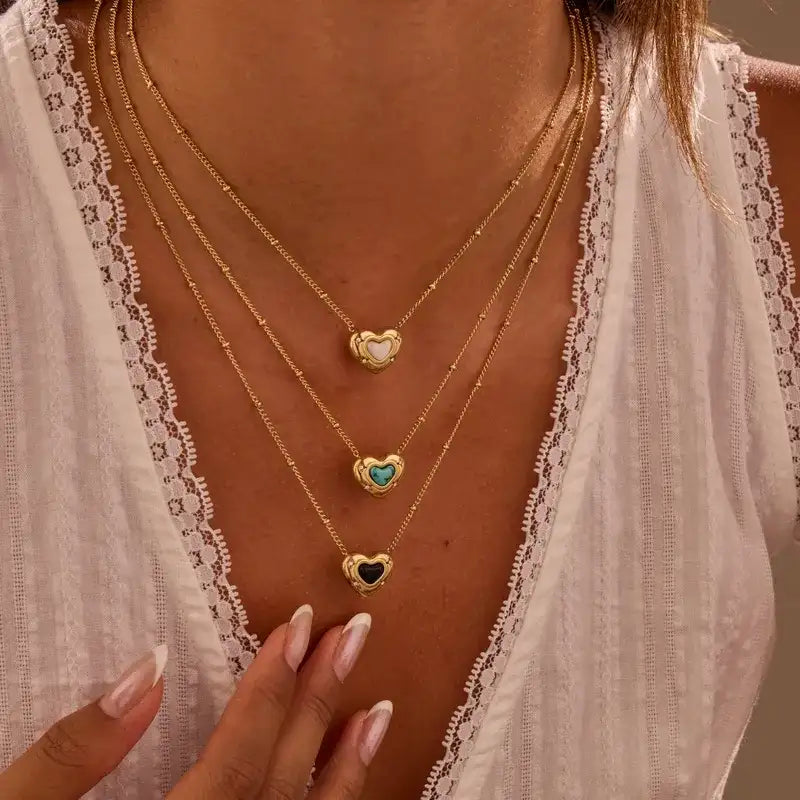 Three gold necklaces with heart-shaped pendants on a person wearing a white lace top.