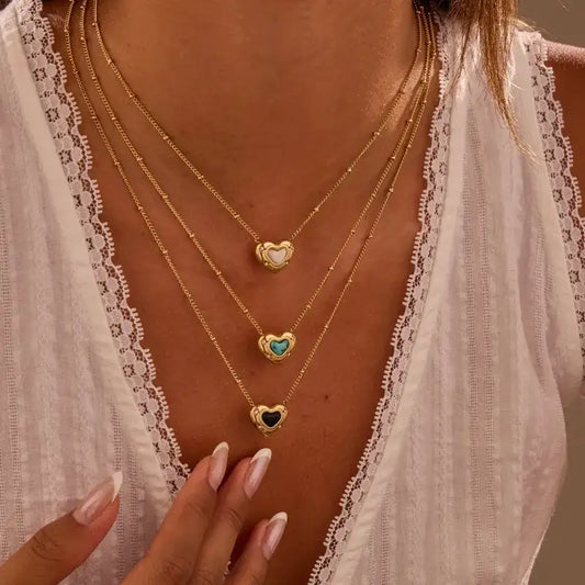 Three gold necklaces with heart-shaped pendants on a person wearing a white lace top.