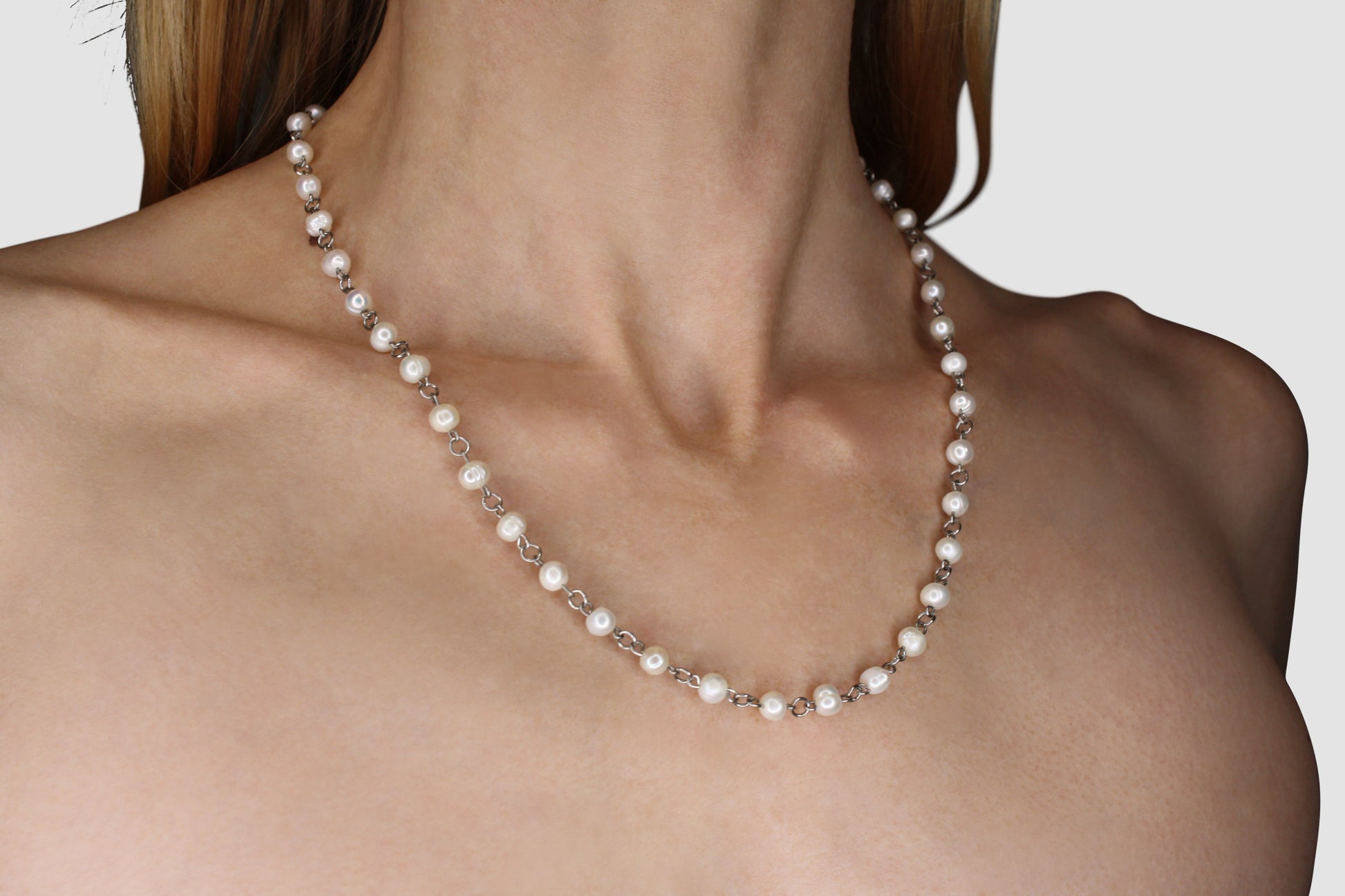 Pearl necklace being worn by a person on a plain background