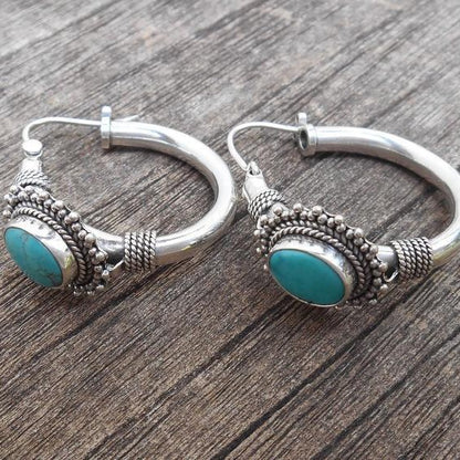 Silver hoop earrings with turquoise stones on a wooden surface