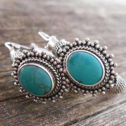Turquoise stone earrings with silver setting on a wooden surface