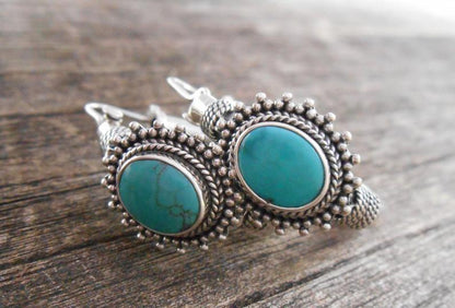 Turquoise stone earrings with silver setting on a wooden surface