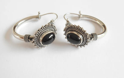 Pair of silver hoop earrings with black stones on a white background