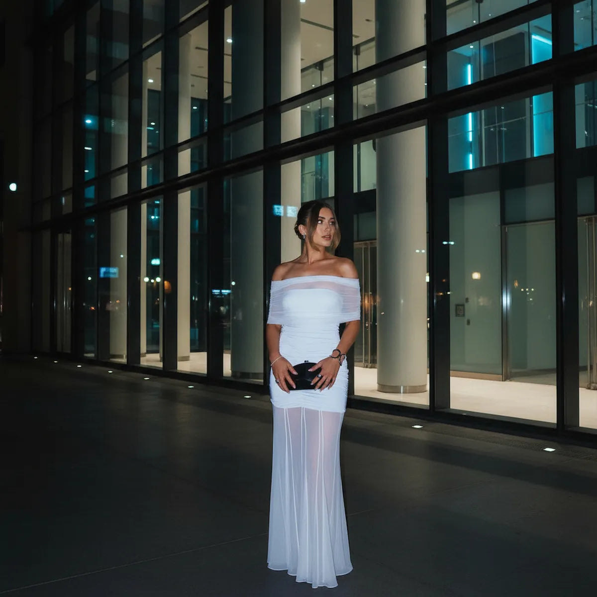 Woman in a  light blue off-shoulder dress standing in front of a modern building at night.