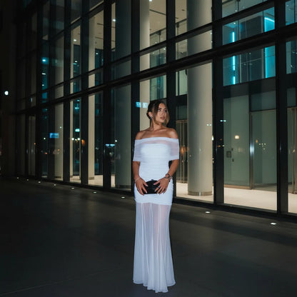 Woman in a  light blue off-shoulder dress standing in front of a modern building at night.