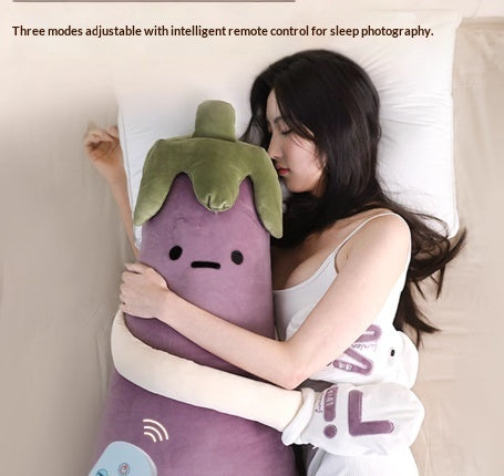 Woman lying on a bed with an eggplant-shaped pillow and remote control for comfort 
