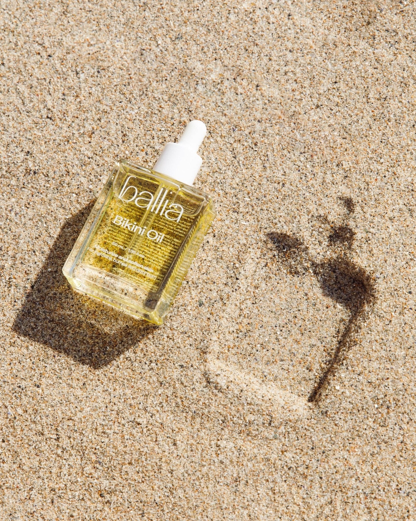 Bottle of Ballia Skinfoil Oil on sand with a shadow