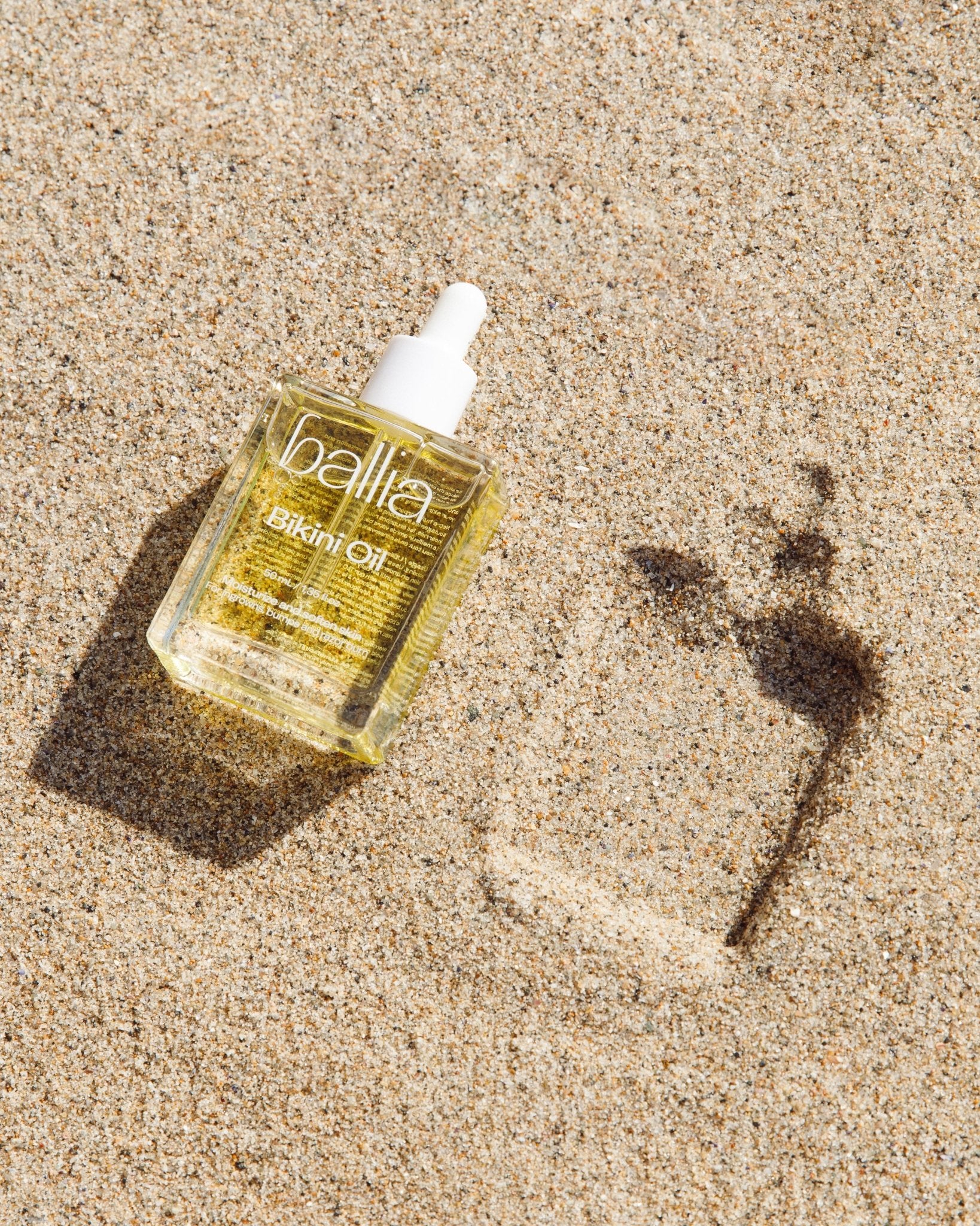 Bottle of Ballia Skinfoil Oil on sand with a shadow