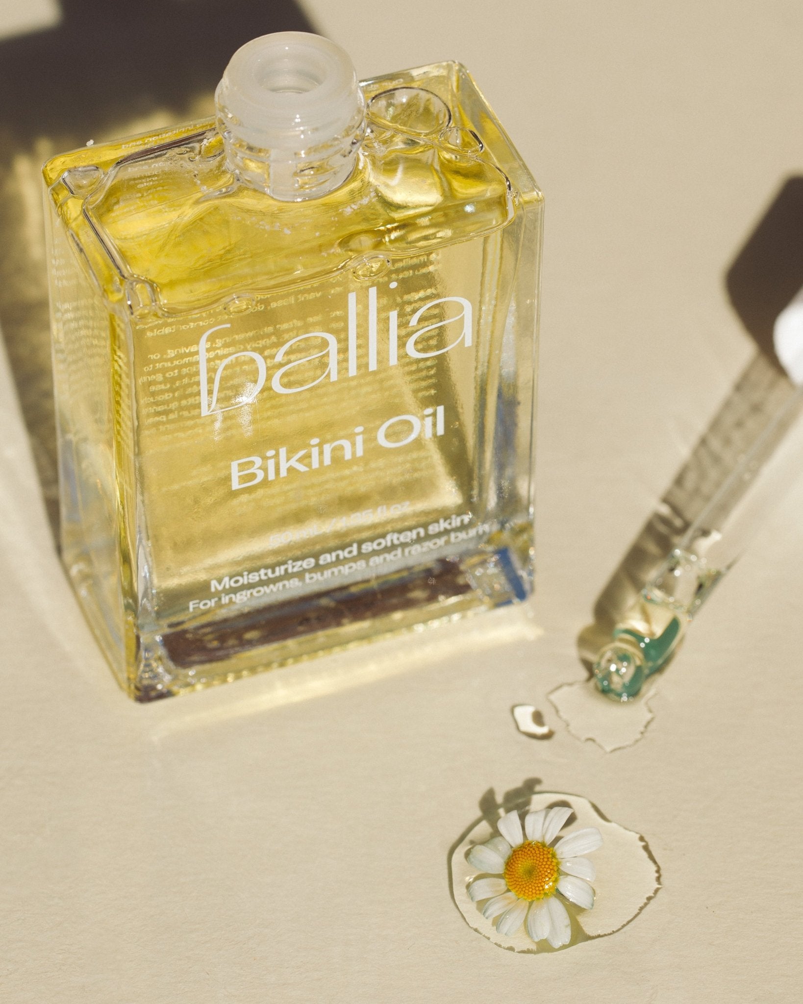 Bottle of Ballia Bikini Oil with a dropper on a beige surface.