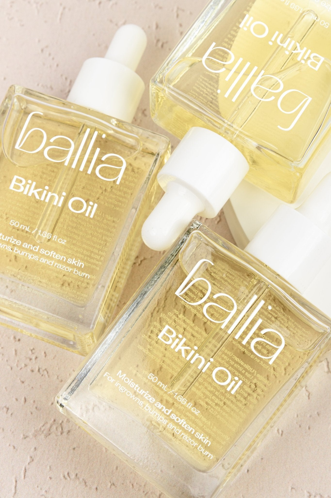 Three bottles of Ballia Bikini Oil on a beige background
