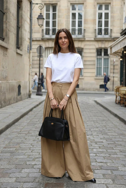 A person wearing a white sleeveless top and very wide-leg pleated tan pants,.