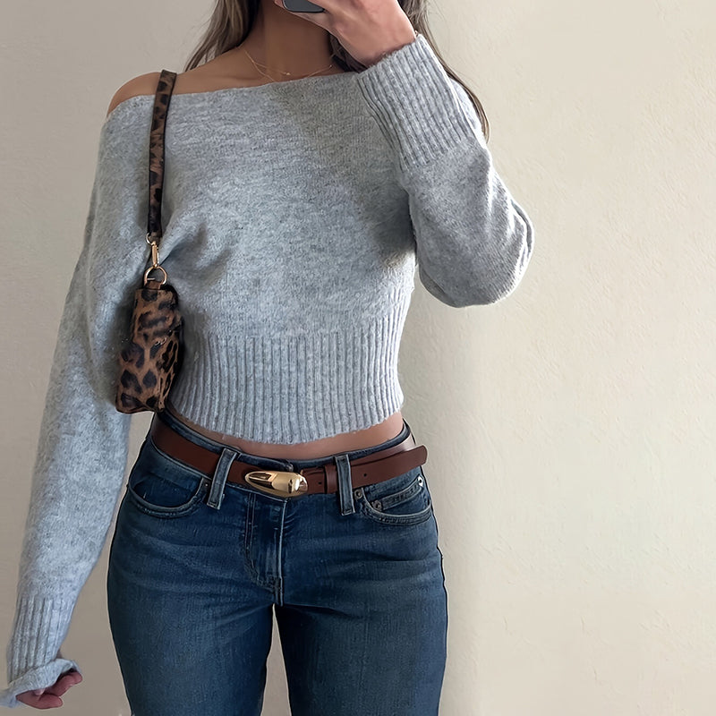 Person wearing a gray off-shoulder sweater and blue jeans with a leopard print bag.
