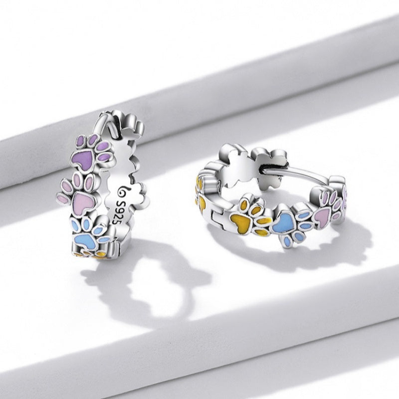 Silver hoop earrings with colorful paw prints on a white surface