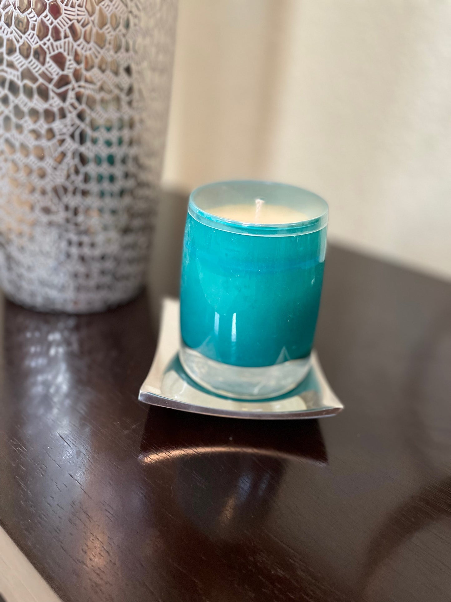 Blue candle in a glass holder on a wooden surface with a textured lamp in the background.
