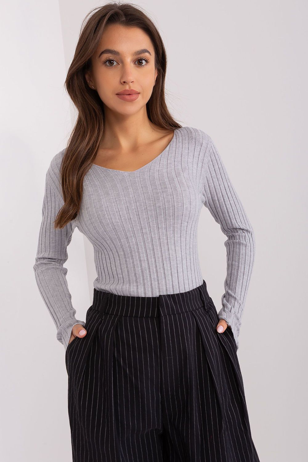 Woman wearing a gray ribbed sweater and black pleated pants
