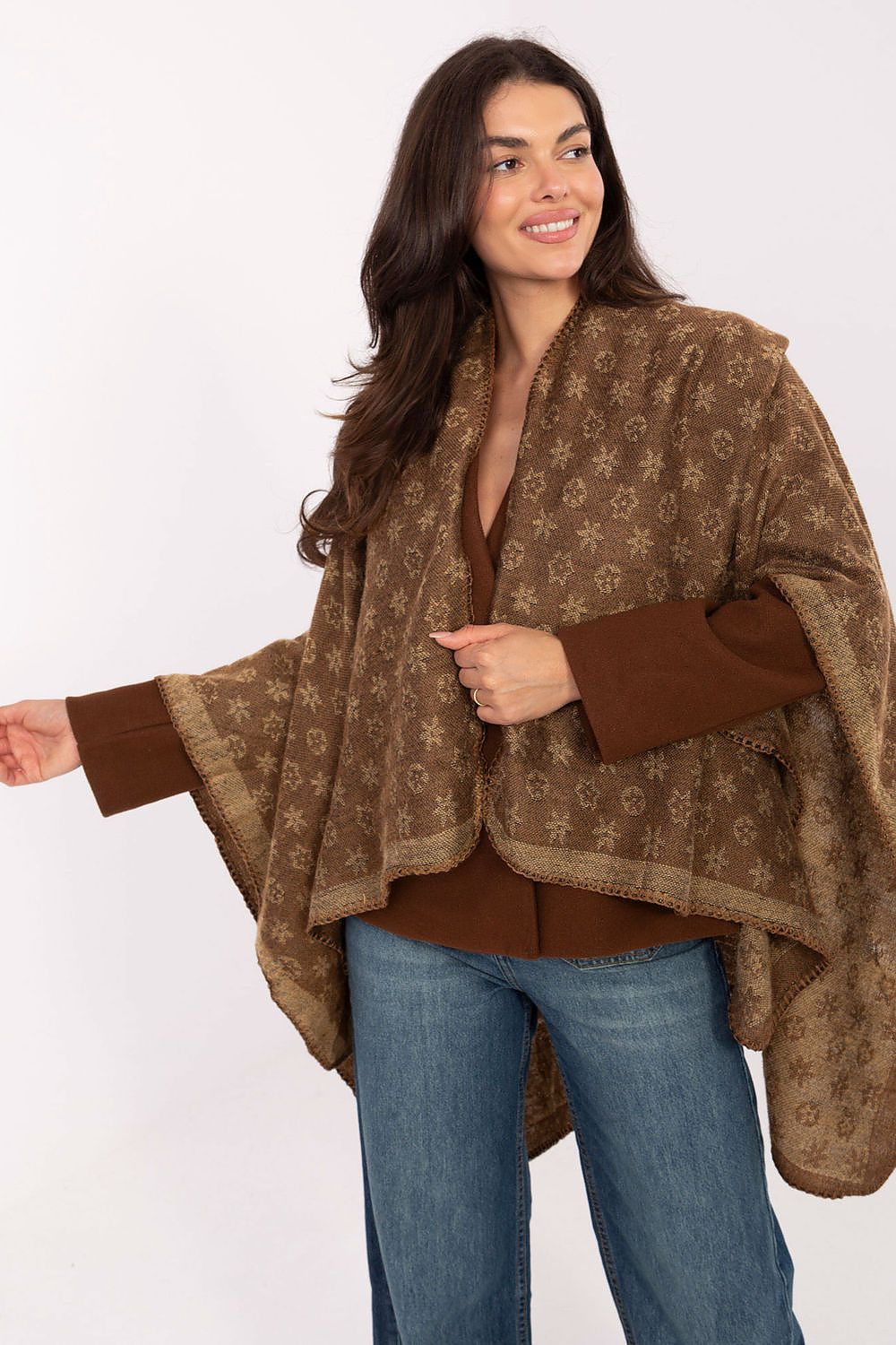 Woman wearing a brown patterned poncho over a brown top and blue jeans 