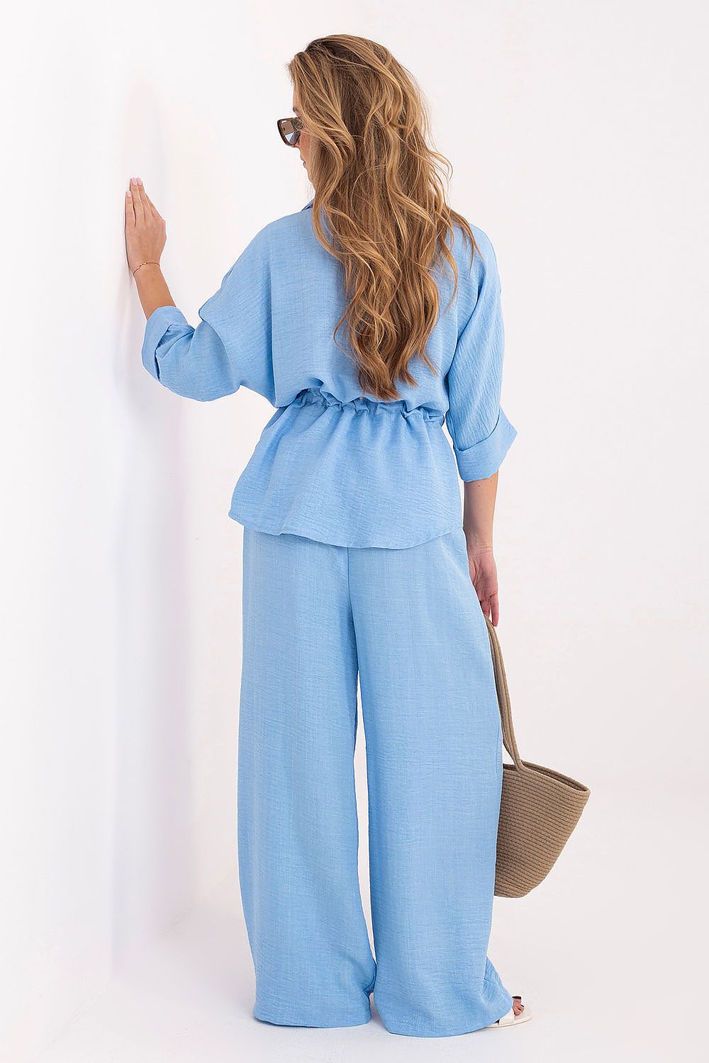 Model wearing wide leg linen blue trousers with pull-on elastic waist, back view styled with sandals