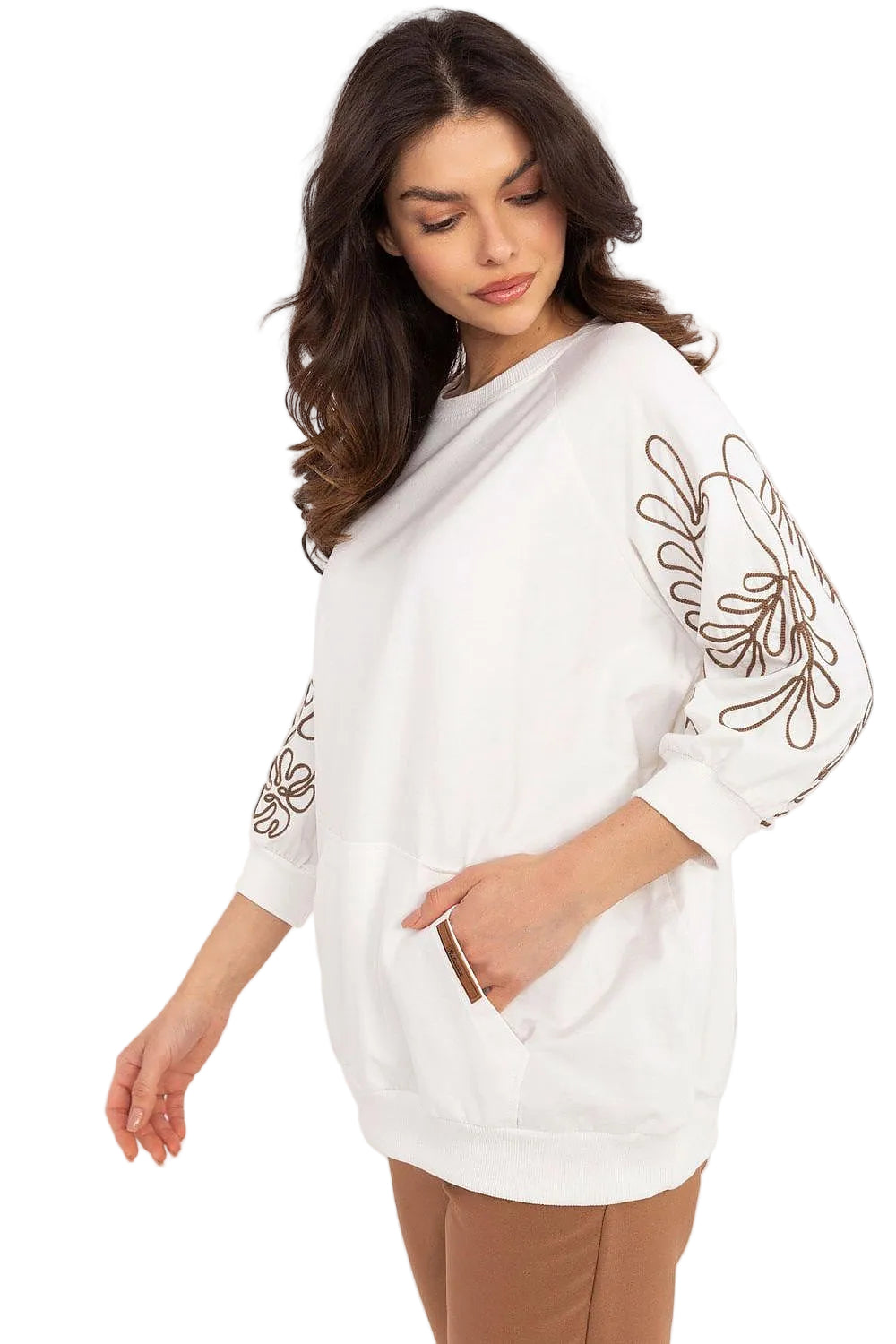 Side view of a model wearing an oversized white pullover sweatshirt with embroidered sleeve details and brown pants.