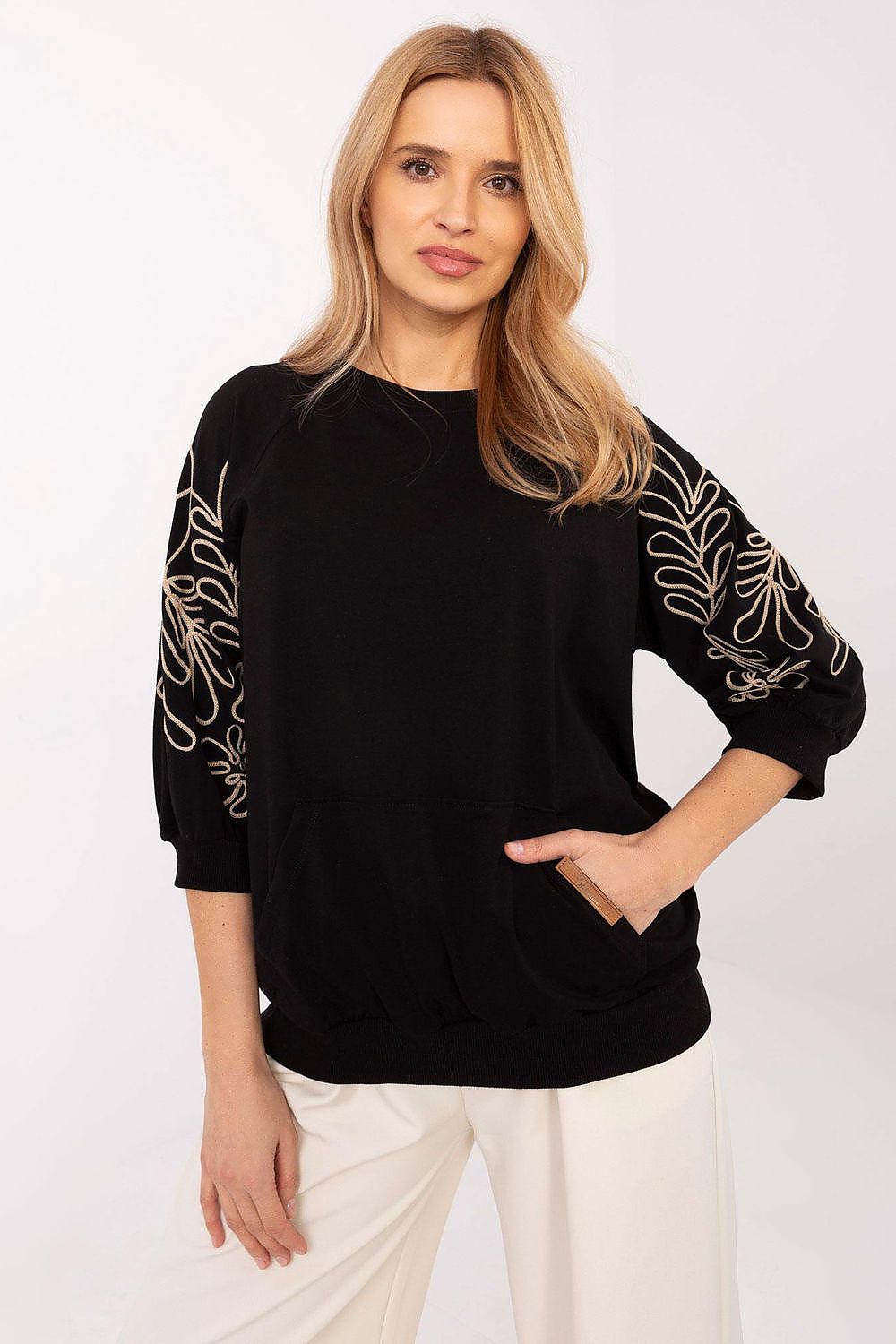 Model wearing a black oversized sweatshirt with white embroidered floral sleeves, paired with cream trousers.
