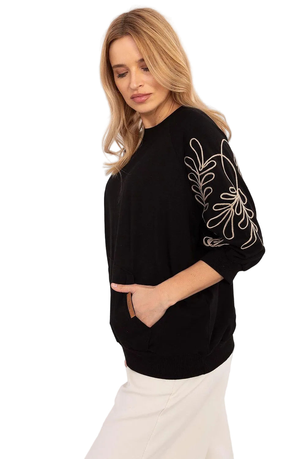 Front view of a model posing in a black crewneck sweatshirt with ornate white embroidery on the sleeves and front pockets.