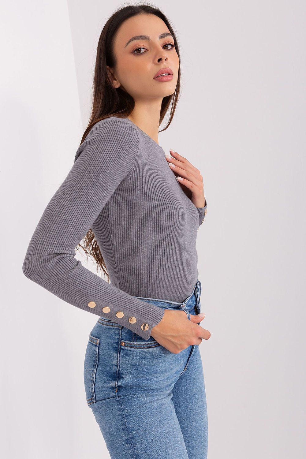 Woman wearing a gray long-sleeve top with button details and blue jeans 