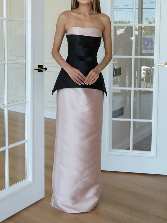 A woman models a strapless formal gown with a black satin bodice and a long blush pink satin skirt.