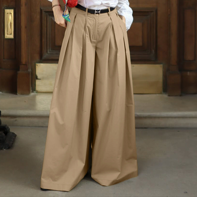 A person wearing high-waisted, wide-leg pleated trousers in a warm tan/beige color, styled with a white shirt and a black belt.