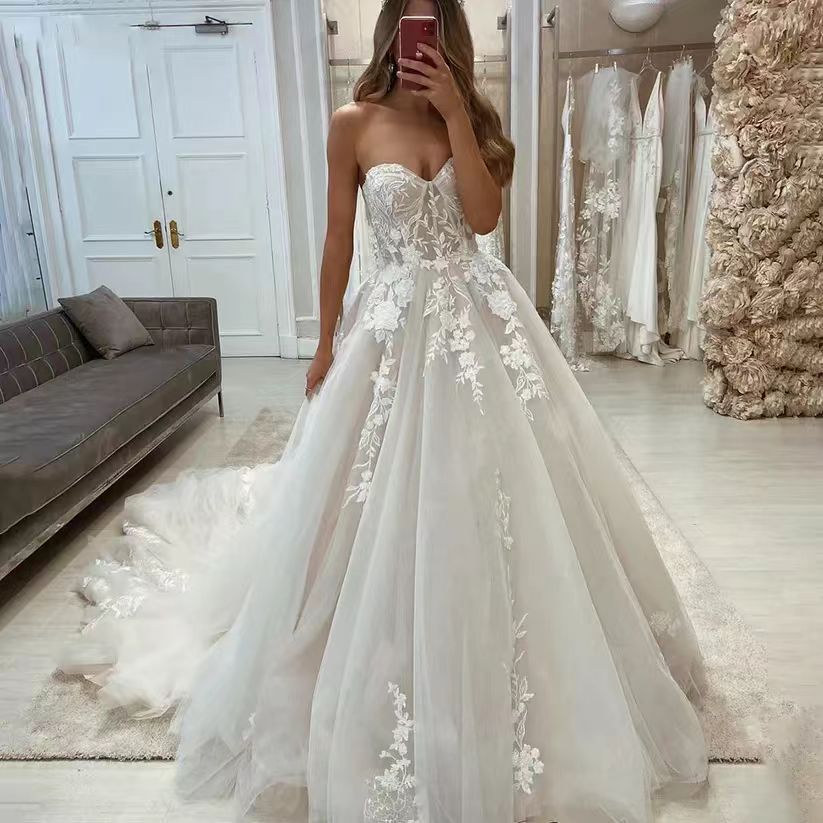Woman in a strapless wedding dress with floral details in a store setting.