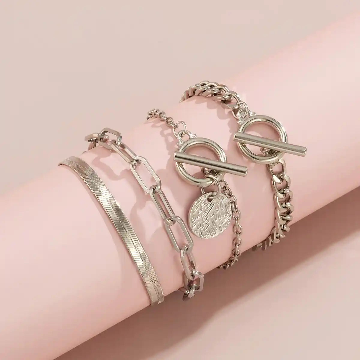 Silver bracelets on a pink arm against a pink background