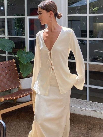Woman wearing a cream-colored outfit standing in front of a window.