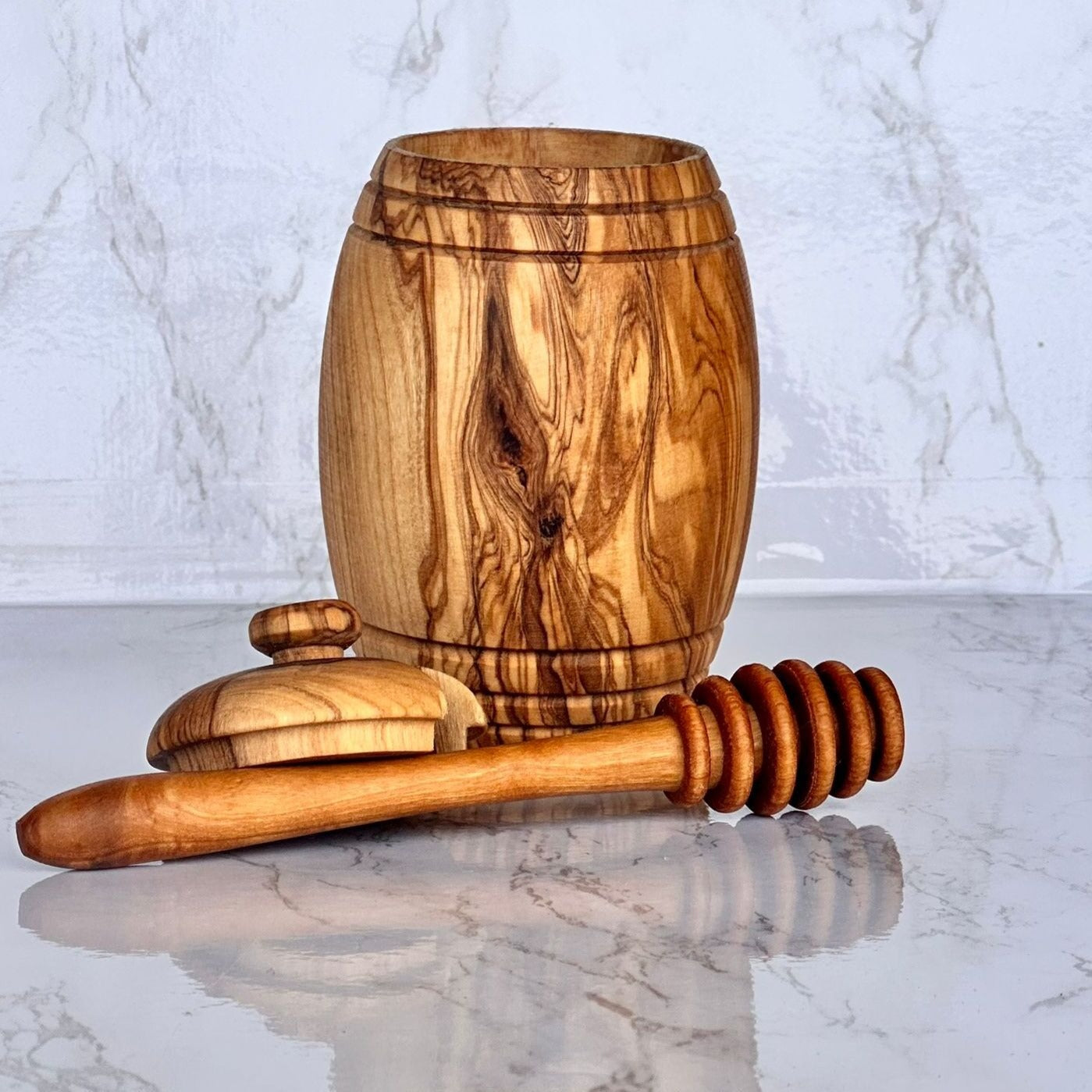 Wooden honey dipper and jar on a marble surface